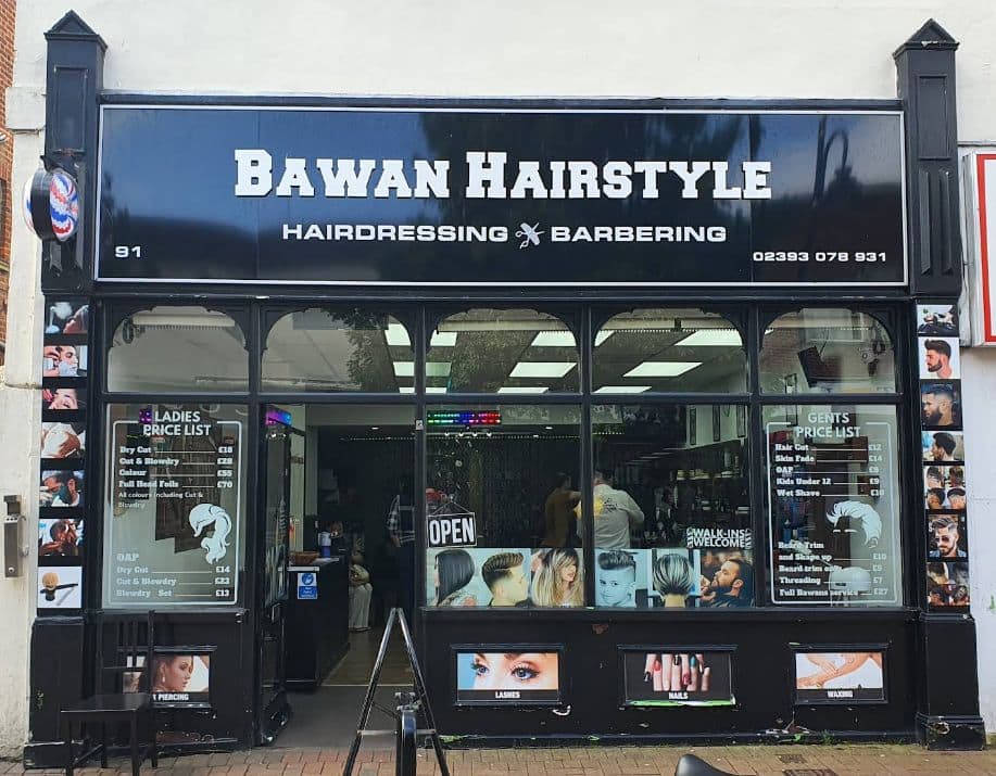 The black shopfront and painted sign of BAWAN HAIRSTYLE at 91 High Street, Gosport, with a traditional red, white and blue barber's pole beside the 