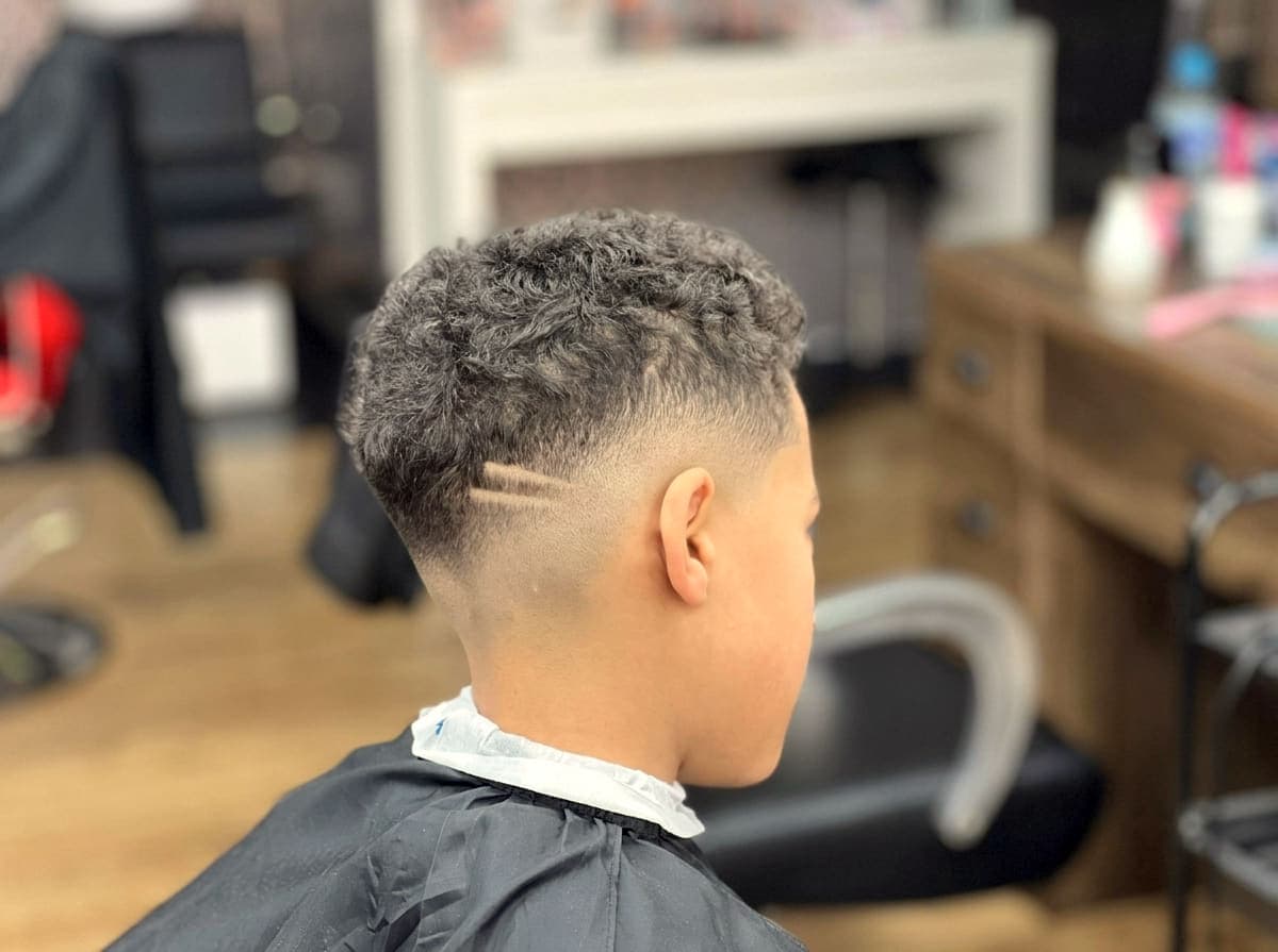 A skin fade blended through curly hair, seen from the side after finishing