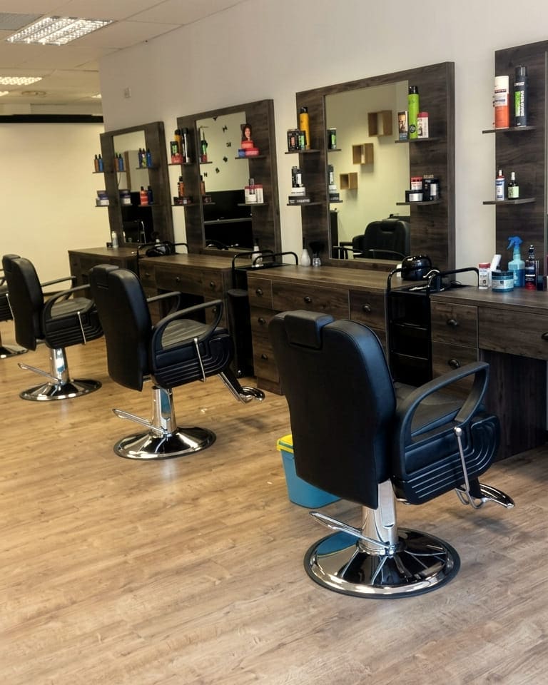 Inside the salon: a row of walnut styling stations with mirrors and black barber chairs on a wood floor
